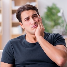 Wincing man holding his cheek in pain