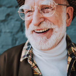 Senior man with glasses smiling in front of brick wall