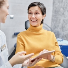 Woman in yellow sweater smiling at dental team member