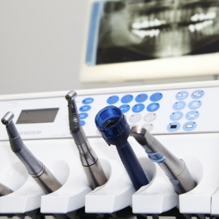 Several dental instruments with x ray of teeth on wall in background