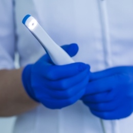 Gloved hands holding a pen like white intraoral camera