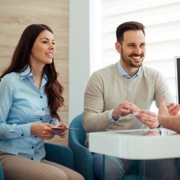 Man and woman sitting across desk from dental team member