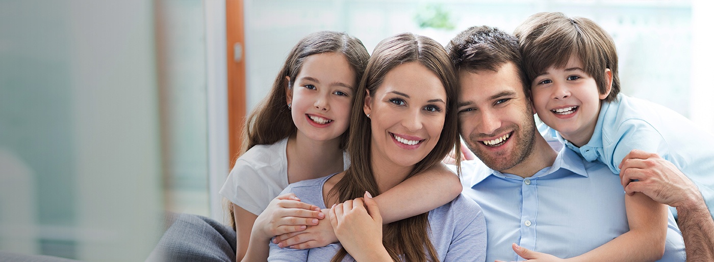 Smiling family of four sitting on couch after visiting dentist in Nepean