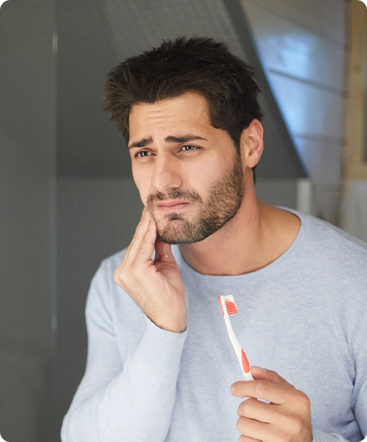 Man holding his toothbrush and wincing while touching his cheek