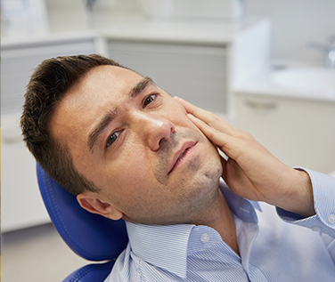 Man in dental chair holding his jaw in pain