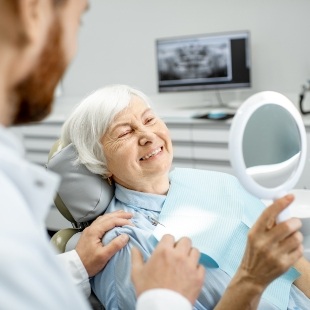 Senior dental patient looking at her smile in mirror after replacing missing teeth in Nepean