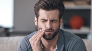 Man sitting on couch and holding his cheek in pain