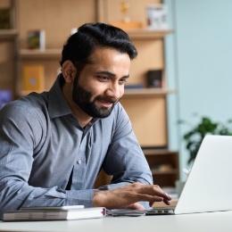 Smiling man sitting at table and using laptop