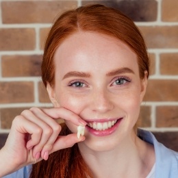 Young woman smiling and holding an extracted tooth