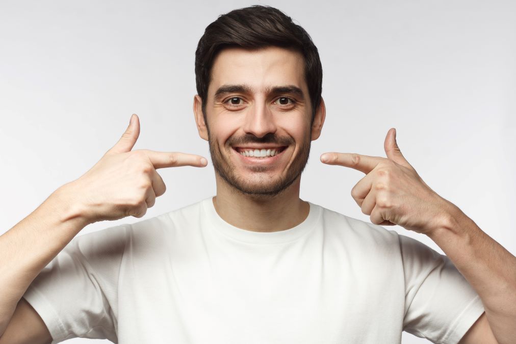 A man smiling and pointing to his teeth.